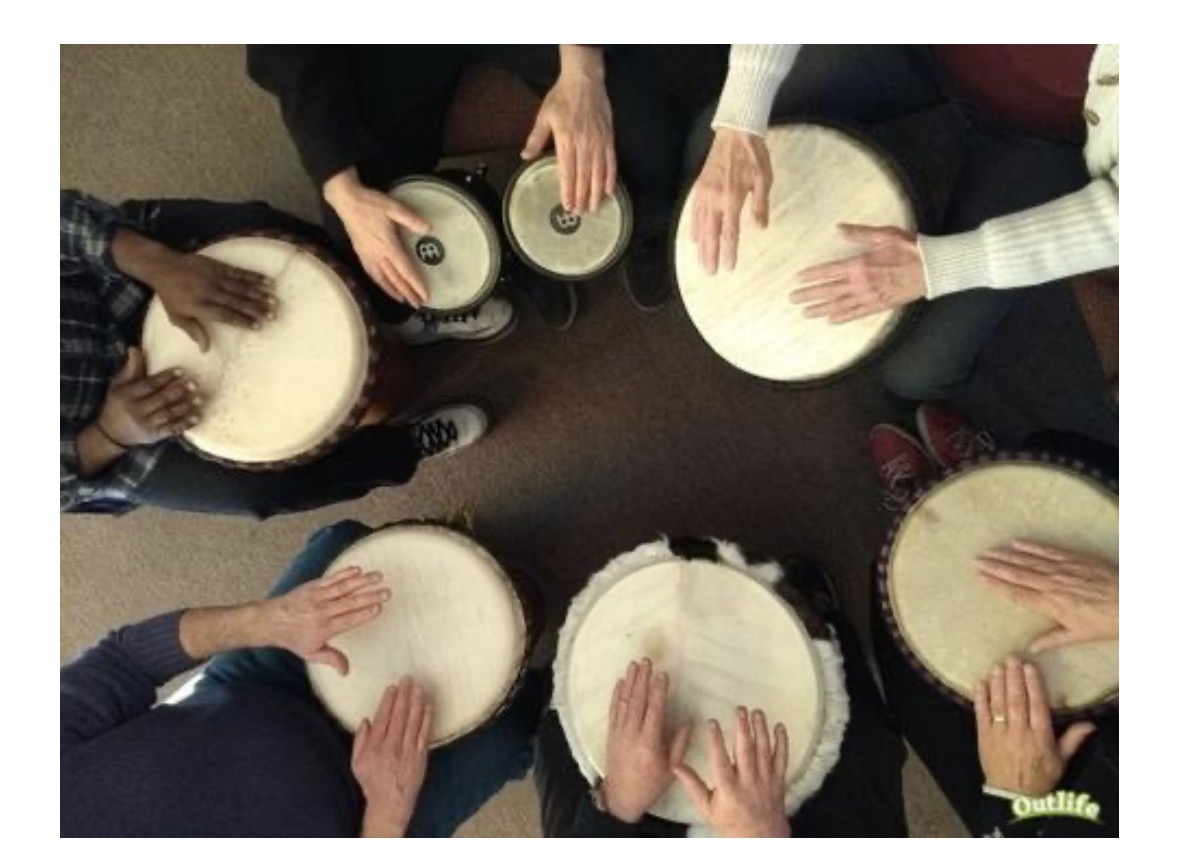 Overhead view of members' hands playing hand drums together in a circle