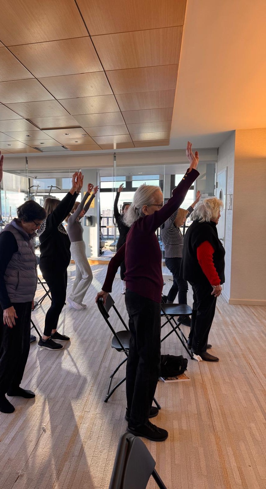 Braygen members raising their arms together during a movement class in a sunlit studio overlooking New York
